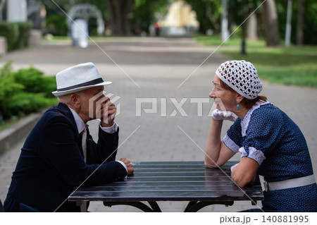 Elderly couple enjoying conversation at a park table during a sunny afternoon in summer 140881995