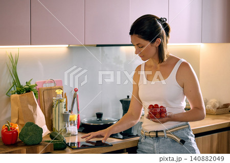 Woman selecting cherry tomatoes while using tablet for smart grocery planning in modern kitchen Woman selecting cherry tomatoes while using tablet for smart grocery planning in modern kitchen 140882049