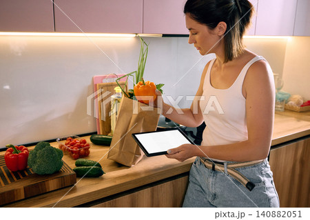 Woman packing fresh vegetables from grocery delivery at home Woman packing fresh vegetables from grocery delivery at home 140882051