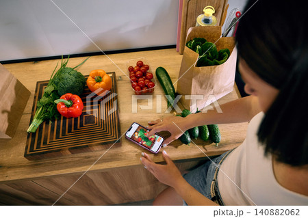 Top view of woman ordering groceries on smartphone in kitchen. 140882062