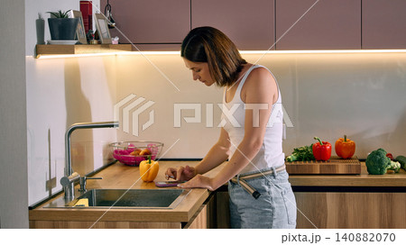 Woman ordering groceries on smartphone near kitchen sink. 140882070