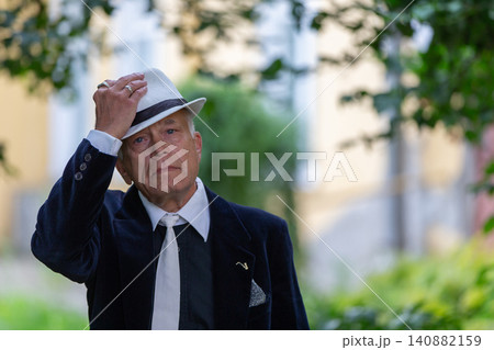 Man adjusts his hat while standing in a lush green garden during a sunny afternoon 140882159