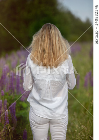 Woman walking through a field of purple flowers on a sunny day surrounded by greenery Woman walking through a field of purple flowers on a sunny day surrounded by greenery 140882346