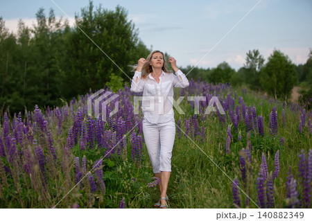 Woman walking through a field of purple flowers on a sunny day in the countryside 140882349