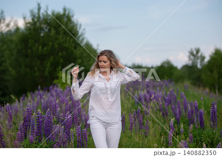 Woman walking through a field of vibrant purple flowers on a sunny afternoon in a natural setting 140882350