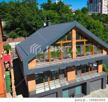House with a gray metal roof and large windows on the facade. Corrugated metal roof and metal roofing. Modern roof made of metal. House with a gray metal roof and large windows on the facade. Corrugated metal roof and metal roofing. Modern roof made of metal. 140883803