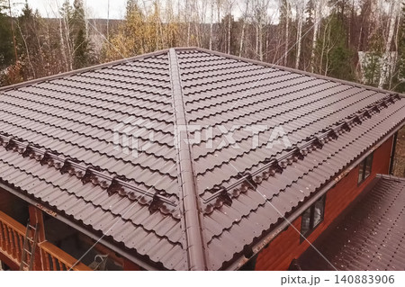 House with a brown metal roof.Corrugated metal roof and metal roofing. Modern roof made of metal. House with a brown metal roof.Corrugated metal roof and metal roofing. Modern roof made of metal. 140883906