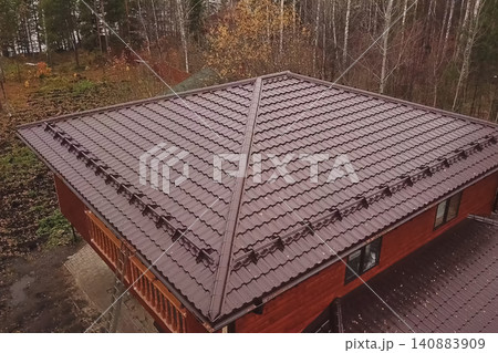 House with a brown metal roof.Corrugated metal roof and metal roofing. Modern roof made of metal. House with a brown metal roof.Corrugated metal roof and metal roofing. Modern roof made of metal. 140883909
