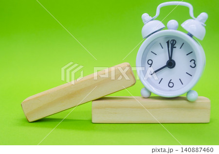 Angled wooden display blocks paired with a vintage alarm clock on a vivid green background for creative product displays. Angled wooden display blocks paired with a vintage alarm clock on a vivid green background for creative product displays. 140887460