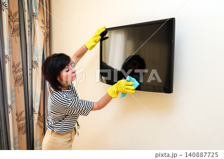 Homemaker in casual clothes wiping dust and dirt off a television screen during routine household cleaning 140887725