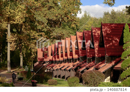 A row of quaint stone and wood structures with distinctive red tiled roofs nestled amongst trees displaying vibrant fall foliage under a bright sky A row of quaint stone and wood structures with distinctive red tiled roofs nestled amongst trees displaying vibrant fall foliage under a bright sky 140887814