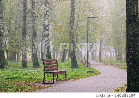 Empty park bench awaits visitors on a misty morning along a winding path 140888104