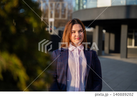 Young businesswoman standing outside a modern office building in an urban corporate district. Career growth and professional success Young businesswoman standing outside a modern office building in an urban corporate district. Career growth and professional success 140889202