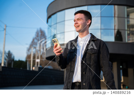 Young man holding a smartphone outside a modern office building while using a mobile banking application. Mobile banking and fintech services for everyday digital finance Young man holding a smartphone outside a modern office building while using a mobile banking application. Mobile banking and fintech services for everyday digital finance 140889216