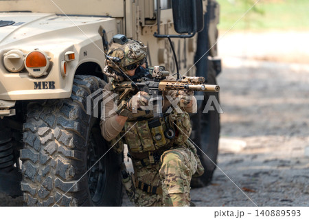 One army man sit and lean on left side front wheel of High Mobility Multipurpose Wheeled Vehicle and point the gun to enemy direction. One army man sit and lean on left side front wheel of High Mobility Multipurpose Wheeled Vehicle and point the gun to enemy direction. 140889593