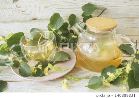 Linden tea in a glass cup with fresh linden flowers, on a wooden background. Medicinal herbal tea. Linden tea in a glass cup with fresh linden flowers, on a wooden background. Medicinal herbal tea. 140889831