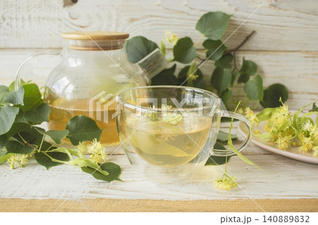 Linden tea in a glass cup with fresh linden flowers, on a wooden background. Medicinal herbal tea. Linden tea in a glass cup with fresh linden flowers, on a wooden background. Medicinal herbal tea. 140889832