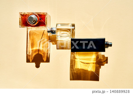 Three luxury perfume bottles casting long shadows on a beige wall 140889928
