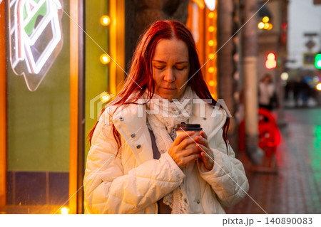 A middle aged Caucasian woman makes a wish with her eyes closed on a rainy evening outside, holding a paper cup of coffee. A magical moment. A middle aged Caucasian woman makes a wish with her eyes closed on a rainy evening outside, holding a paper cup of coffee. A magical moment. 140890083