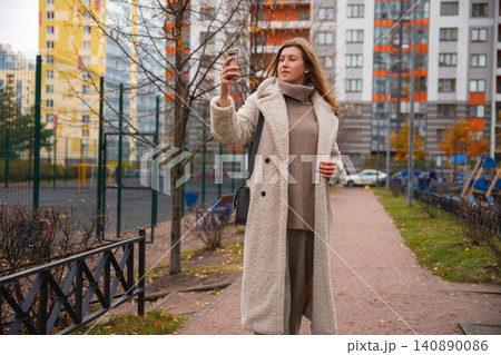 Caucasian woman in a coat surfs news on her smartphone, writes message on social media, takes selfie photo with smartphone. Caucasian woman in a coat surfs news on her smartphone, writes message on social media, takes selfie photo with smartphone. 140890086