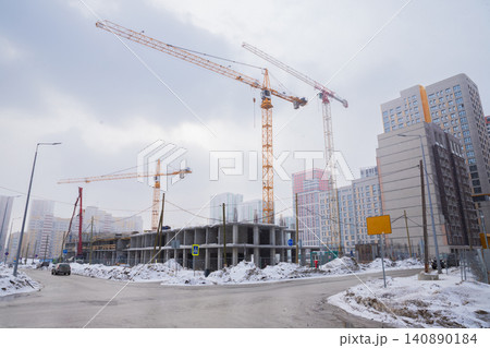 Tower cranes at yellow construction site of new residential buildings. Winter cityscape with concrete structure in snowy city. Urban development and real estate investment concept. Tower cranes at yellow construction site of new residential buildings. Winter cityscape with concrete structure in snowy city. Urban development and real estate investment concept. 140890184