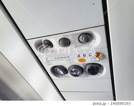Passenger airplane overhead console with ventilation air nozzles and reading light buttons. Aviation safety panel with seat row number indication inside commercial aircraft cabin. Passenger airplane overhead console with ventilation air nozzles and reading light buttons. Aviation safety panel with seat row number indication inside commercial aircraft cabin. 140890193