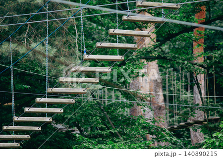 Suspension rope bridge with wooden steps in an outdoor adventure park Suspension rope bridge with wooden steps in an outdoor adventure park 140890215