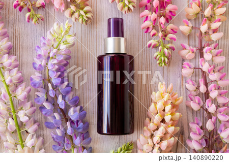 Cosmetic spray bottle with flower on wooden background. Skin care product bottle surrounded by spring lupine bloom. Natural organic beauty cosmetic branding concept for spa and wellness. 140890220