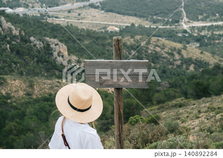 Woman in straw hat reading blank signboard in mountainous landscape 140892284