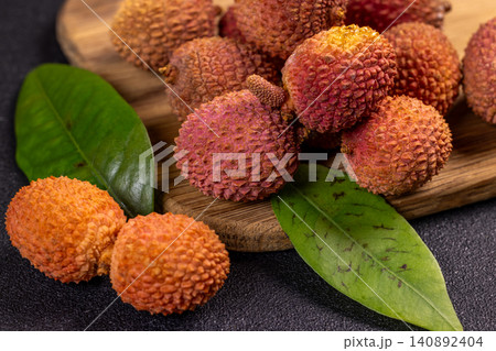 Fresh lychees with leaves resting on wooden cutting board 140892404
