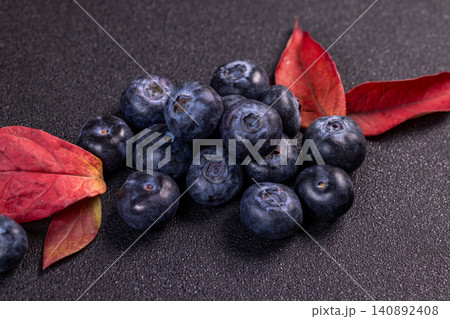 Fresh blueberries and red autumn leaves creating a vibrant contrast on dark background Fresh blueberries and red autumn leaves creating a vibrant contrast on dark background 140892408