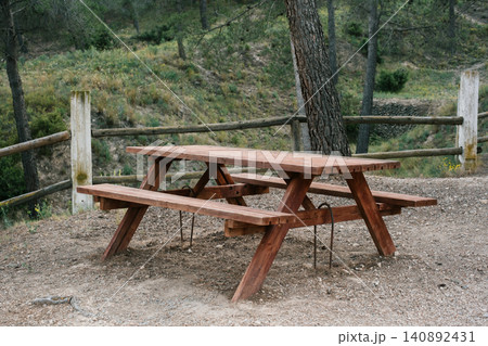 Rustic wooden picnic table in serene forest setting with lush greenery Rustic wooden picnic table in serene forest setting with lush greenery 140892431