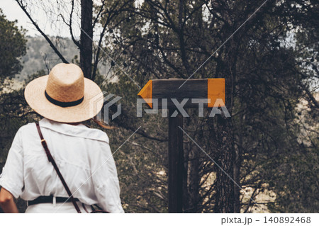 Woman in straw hat exploring nature trail with wooden sign in forest Woman in straw hat exploring nature trail with wooden sign in forest 140892468
