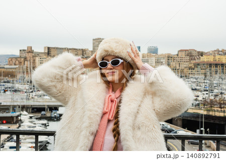 Stylish woman in fur coat and sunglasses by marina with cityscape view 140892791
