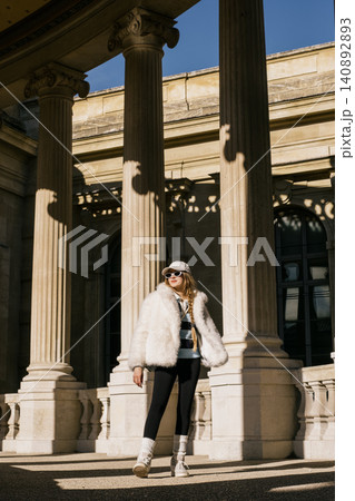 Stylish woman in fur coat and sunglasses walking by classical columns on a sunny day 140892893