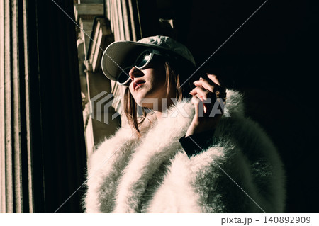 Fashionable woman in sunglasses and fluffy coat standing in urban setting Fashionable woman in sunglasses and fluffy coat standing in urban setting 140892909