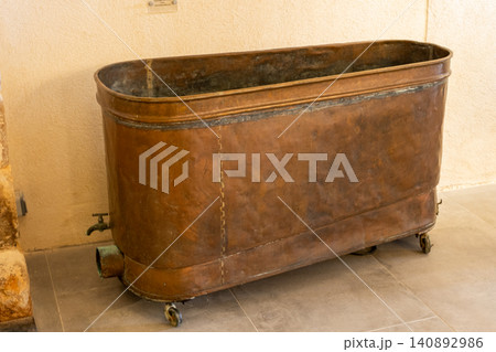 Vintage copper bathtub on wheels displayed in rustic room setting reflecting historical elegance 140892986
