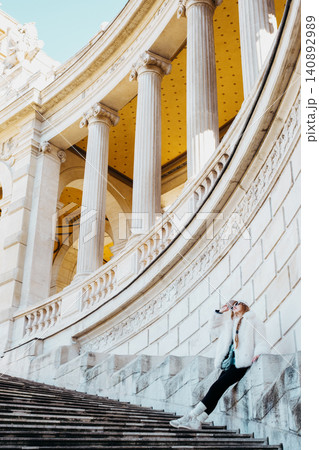 Woman relaxing on architectural steps with classical columns in elegant urban setting Woman relaxing on architectural steps with classical columns in elegant urban setting 140892989