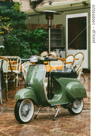 Vintage green scooter in cozy outdoor cafe setting on a rainy day Vintage green scooter in cozy outdoor cafe setting on a rainy day 140893020