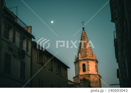 Historic church steeple at dusk with moon in the sky against urban building silhouettes 140893043