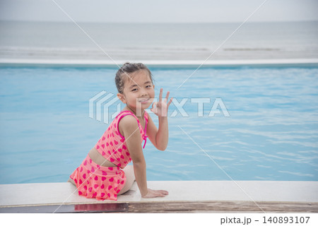Toddler girl Kid swim playful in swimming pool summer time with pink swimwear in blue water at hotel swimming pool outdoor. Happy girl swim playful water splash with happiness on summer vacation Toddler girl Kid swim playful in swimming pool summer time with pink swimwear in blue water at hotel swimming pool outdoor. Happy girl swim playful water splash with happiness on summer vacation 140893107