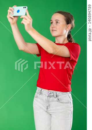 Teenage girl taking photo or scanning QR code in front of green screen Teenage girl taking photo or scanning QR code in front of green screen 140894789