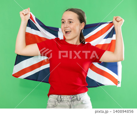 Teenage girl in red T-shirt and jeans with large flag of United Kingdom posing on green background. Chroma key compositing Teenage girl in red T-shirt and jeans with large flag of United Kingdom posing on green background. Chroma key compositing 140894856