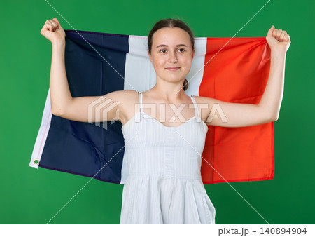 Teen girl dressed in summer dress posing against green background waving France flag Teen girl dressed in summer dress posing against green background waving France flag 140894904