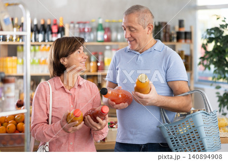 Mature couple hold white plastic bottles and choose consider juice fruit in store Mature couple hold white plastic bottles and choose consider juice fruit in store 140894908