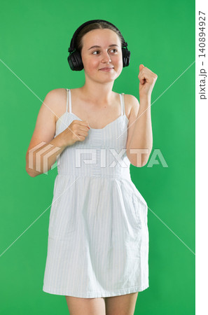 Passionate teenage girl listening and dancing to music on headphones on green background. Chroma key compositing Passionate teenage girl listening and dancing to music on headphones on green background. Chroma key compositing 140894927