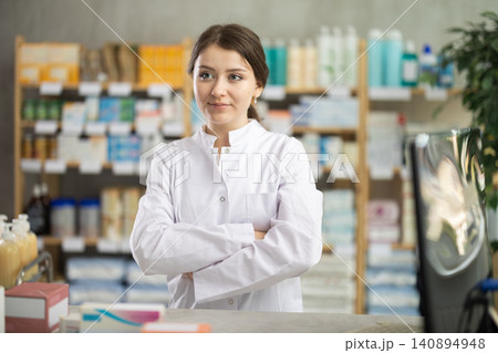 Confident female pharmacist standing behind counter with arms crossed Confident female pharmacist standing behind counter with arms crossed 140894948