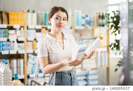 Girl in summer clothes choosing skin cream at drugstore Girl in summer clothes choosing skin cream at drugstore 140895037