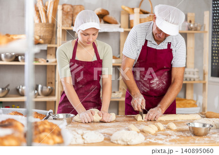 Male and female bakers kneading and cutting dough 140895060