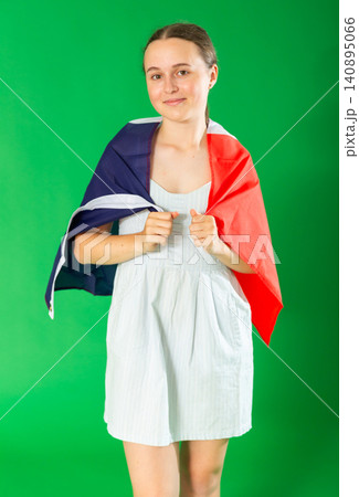 Teenage girl in a white dress with large flag of France posing on green background. Chroma key compositing 140895066